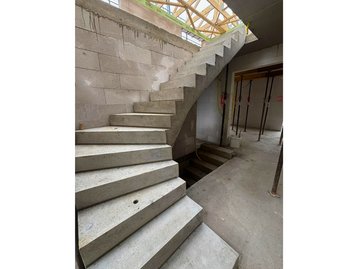 Die geschwungene Rohbau-Betontreppe im Erdgeschoss führt nach oben in das Dachgeschoss des Einfamilienhauses.