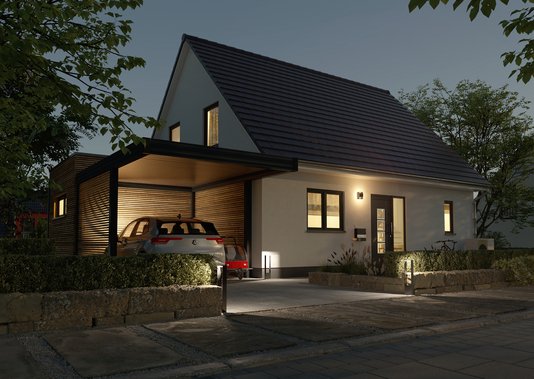 Modernes Einfamilienhaus mit Satteldach und Carport bei Abendbeleuchtung. Auffahrt mit geparktem Auto, gepflegter Vorgarten und warm beleuchtete Fassade.