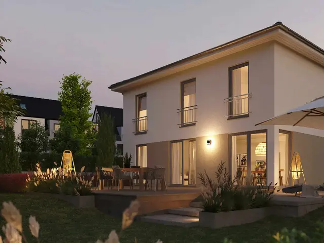 Modernes zweigeschossiges Einfamilienhaus in Massivbauweise bei Abenddämmerung. Große Fenster, stilvolle Außenbeleuchtung, Terrasse mit Sitzbereich und Sonnenschirm, gepflegter Garten mit Pflanzen und Rasen. Stimmungsvolle Darstellung eines hochwertigen Wohnhauses.