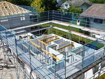 Luftaufnahme der eingerüsteten Baustelle des Einfamilienhauses in Straßlach aus der Vogelperspektive.