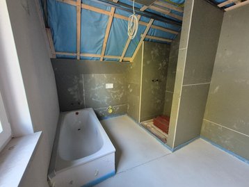 Badezimmer im Dachgeschoss mit Dachschräge, freigelegter Dachisolierung, eingebauter Badewanne, Estrichboden und Trockenbauwänden.