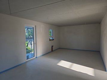 Hell verputzte Innenräume mit frisch gegossenem Estrich und großen Fenstern im Neubau in Niederaichbach.
