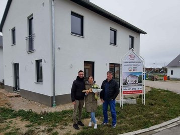 Hausübergabe eines neu gebauten, zweistöckigen Massivhauses durch die Trausnitz Massivhaus Bau GmbH an das glückliche Bauherrenpaar mit Holzschlüssel und Bauschild