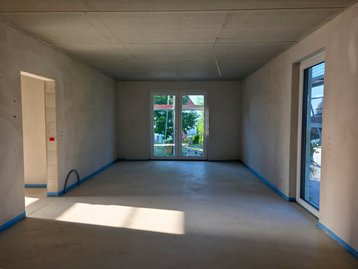 Heller, verputzter Wohnbereich im Erdgeschoss des Flair 110 mit frisch gegossenem Estrich und Blick durch die Terrassentür.