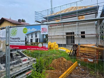 Das offizielle Bauschild vor dem fertig aufgestellten Rohbau des Massivhauses Flair 152 RE in Straßlach.